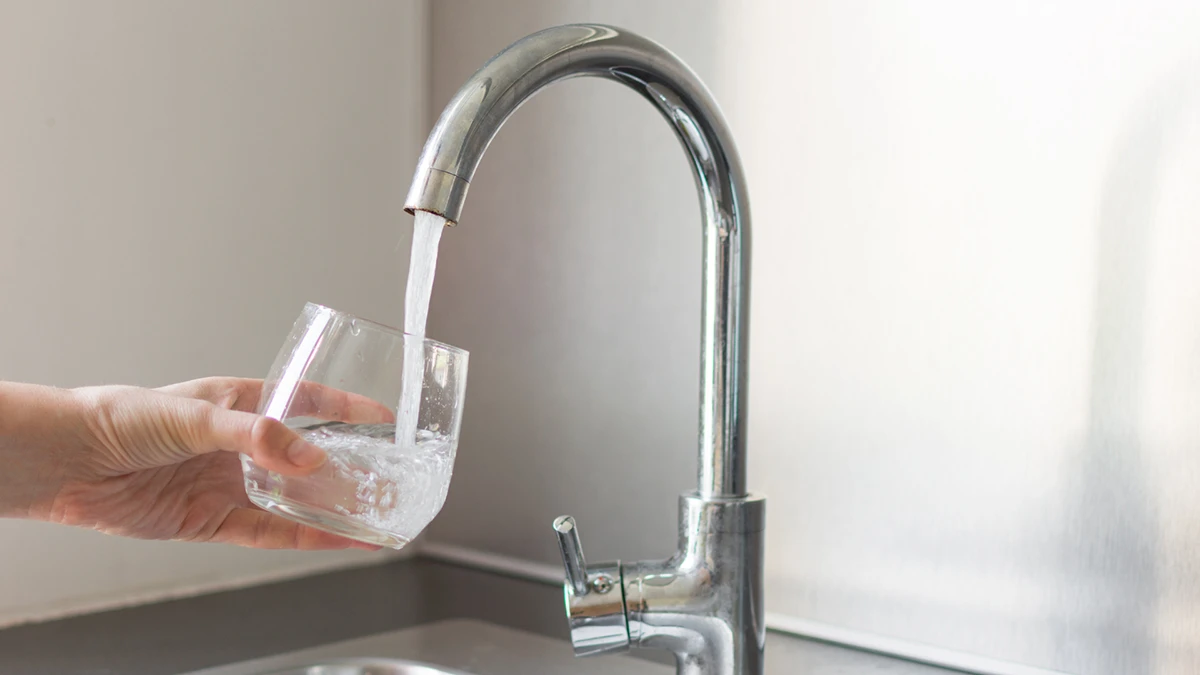 A person holds a glass of water under a running faucet, preparing to drink.