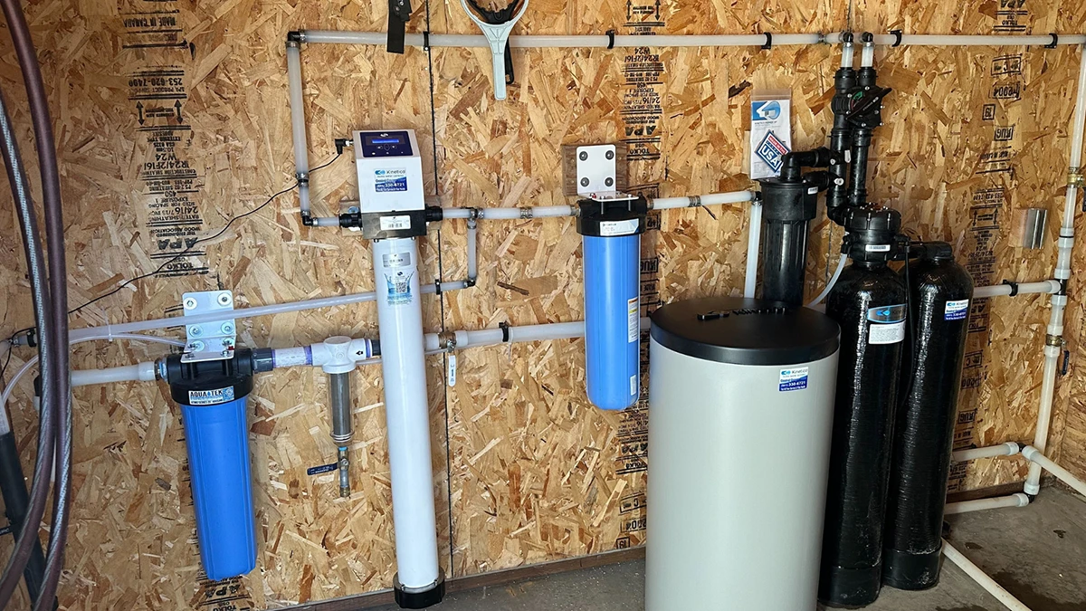 Water softener and water heater installed in a utility room, showcasing plumbing and appliance setup for home water treatment. Water softener and water heater installed in a utility room, showcasing plumbing and appliance setup for home water treatment.
