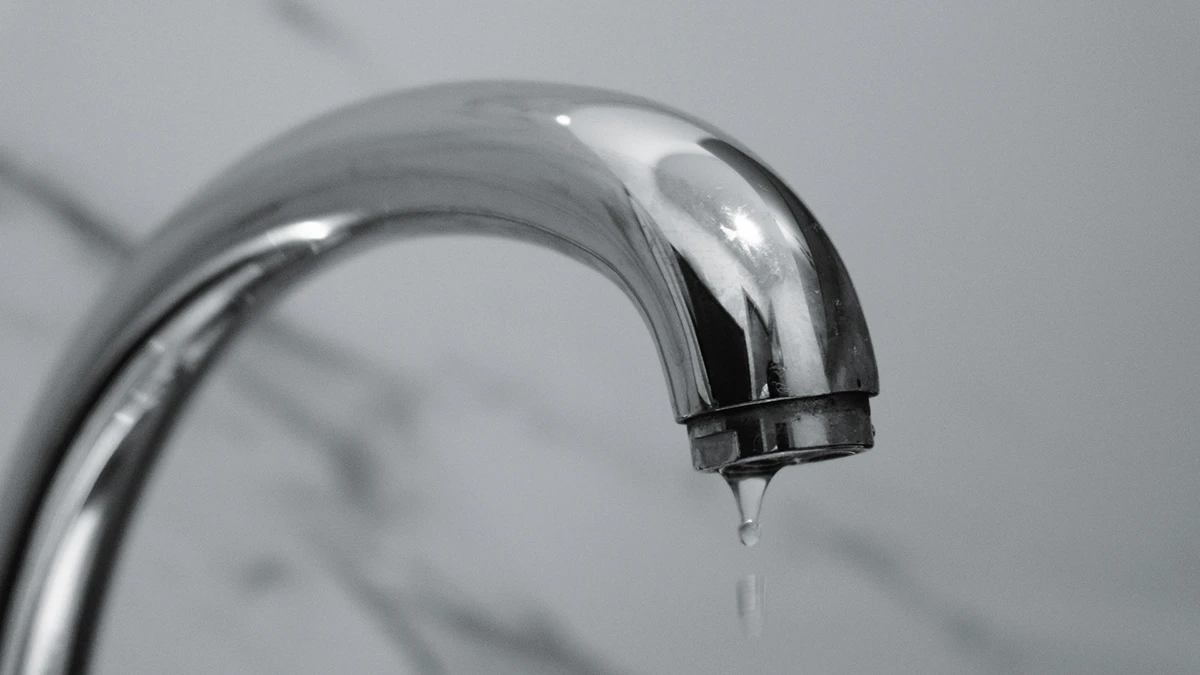 Close-up of a silver faucet against a blurred gray background, releasing a single droplet of water. The scene evokes a calm and minimalist atmosphere. Close-up of a silver faucet against a blurred gray background, releasing a single droplet of water. The scene evokes a calm and minimalist atmosphere.