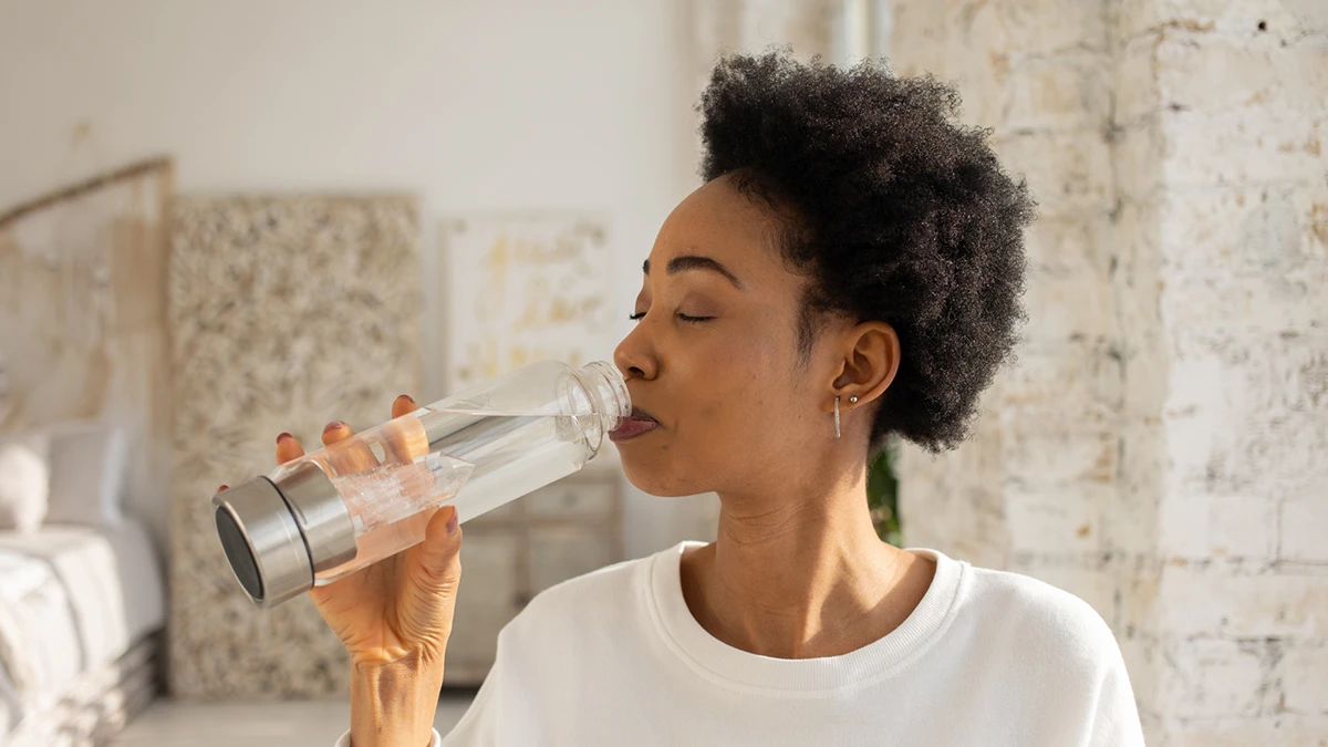 A woman sipping from a water bottle while standing outdoors, enjoying hydration during an activity.