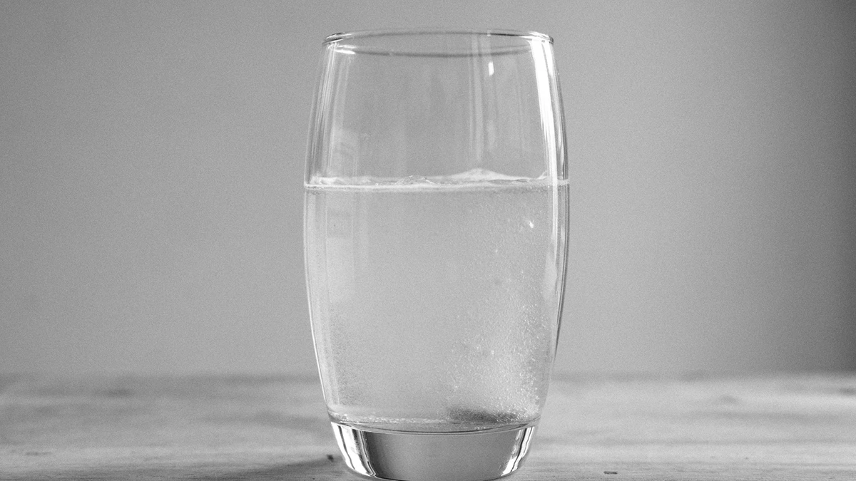 A clear glass of water placed on a wooden table, reflecting light from nearby windows.